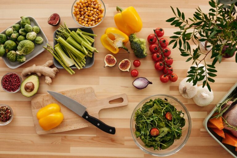 Overhead view of fresh colorful vegetables, chickpeas, and whole food ingredients on a wooden kitchen counter for clean eating and metabolic health.