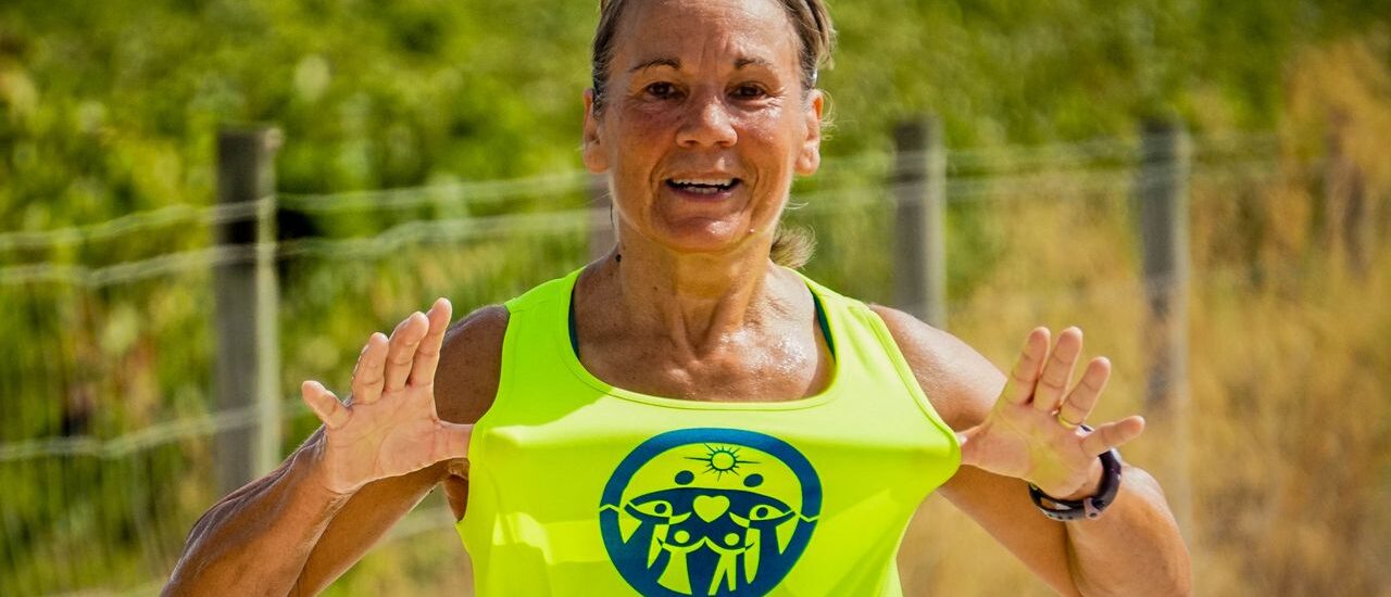Active middle-aged woman smiling while jogging outdoors on a sunny day, representing healthy aging and fitness for mybestfit.net