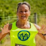 Active middle-aged woman smiling while jogging outdoors on a sunny day, representing healthy aging and fitness for mybestfit.net